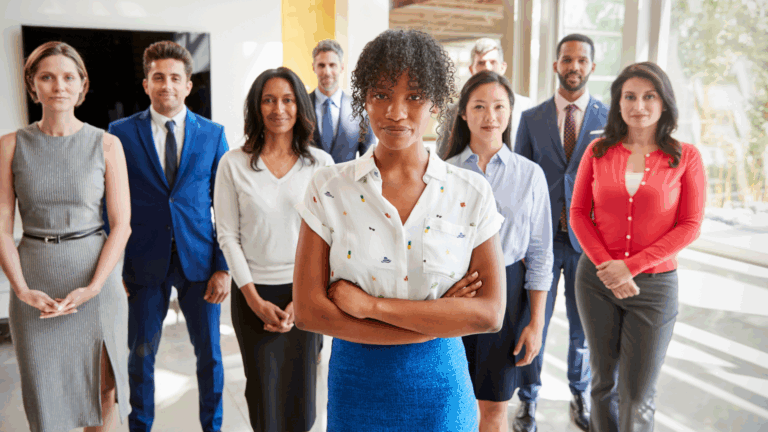 A group of diverse professionals standing together in an office environment, with one woman in the foreground.