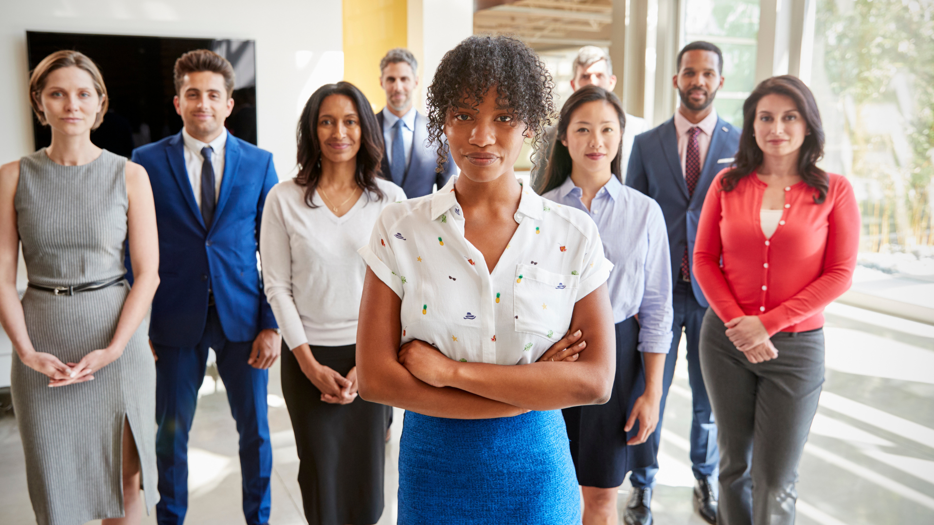 A group of diverse professionals standing together in an office environment, with one woman in the foreground.