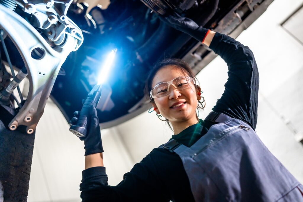 Female mechanic inspecting car with flashlight in workshop
