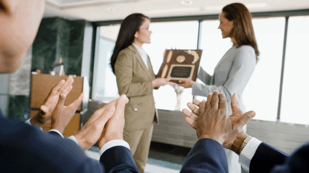 Two women exchanging an award during a presentation ceremony in an office setting.