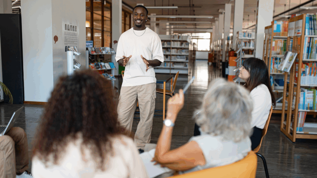 Individual standing and speaking to a small group of people seated in a library setting.