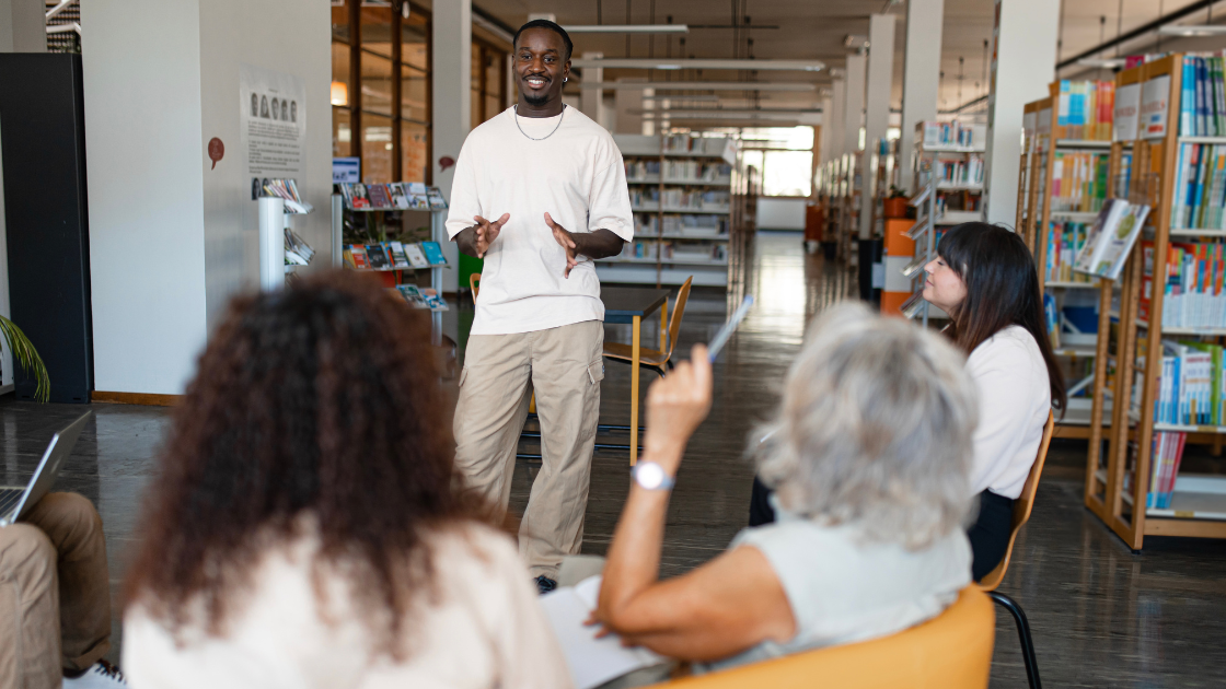 Individual standing and speaking to a small group of people seated in a library setting.