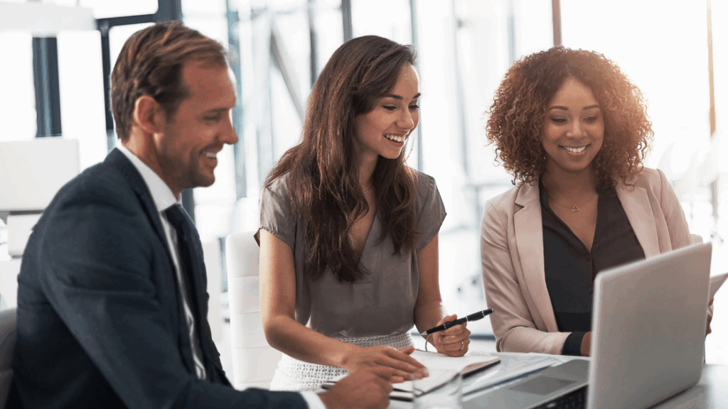 Three professionals engaged in a discussion while working on a laptop during a meeting.