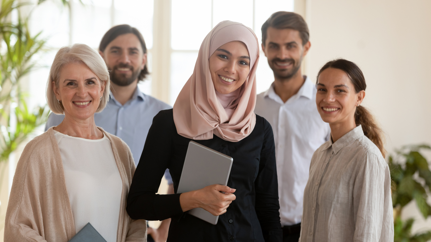 A diverse team smiles together in a bright office, supporting diversity and inclusion through healthier workplace culture and intentional leadership action.