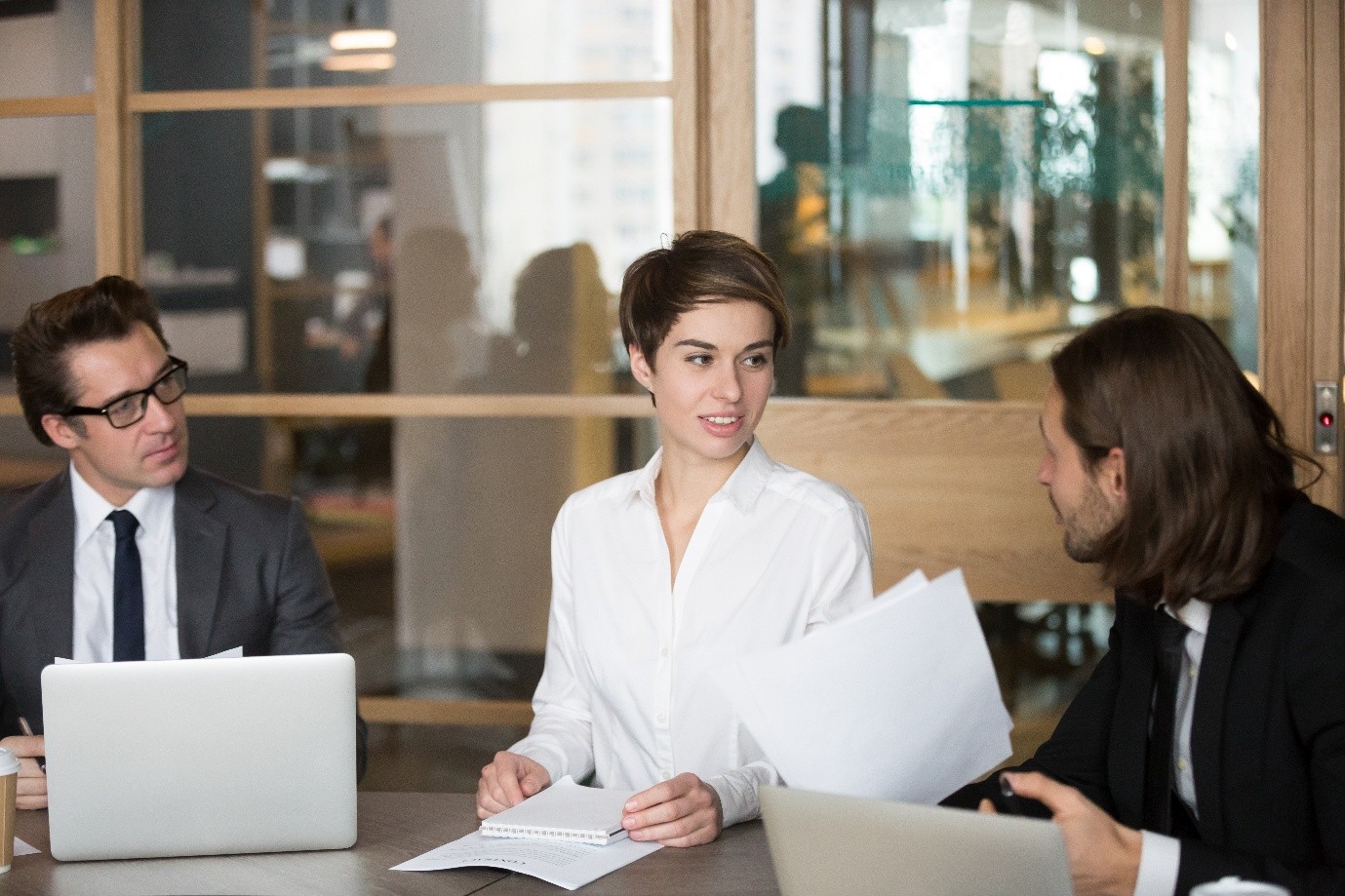Conference room scene featuring a woman in a white shirt and two men in suits discussing HR compliance policies at The Atrium LLC in California