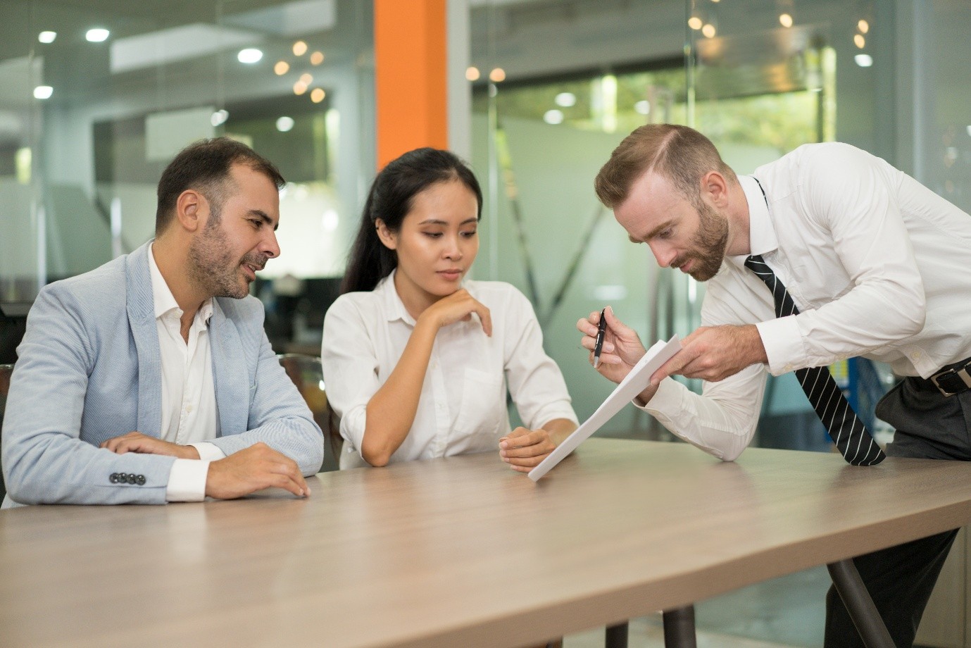 Three professionals engaged in a business meeting at a conference table, discussing documents.