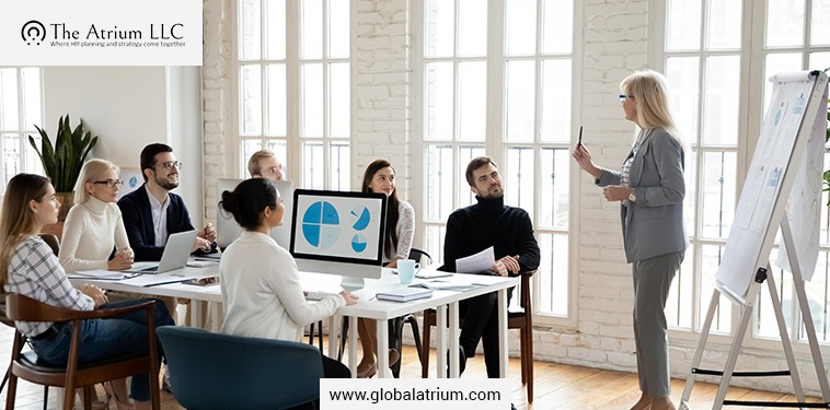A leadership training session for HR training in nuclear plants, with a presenter explaining compliance, while a team reviews slides in a bright office meeting room.