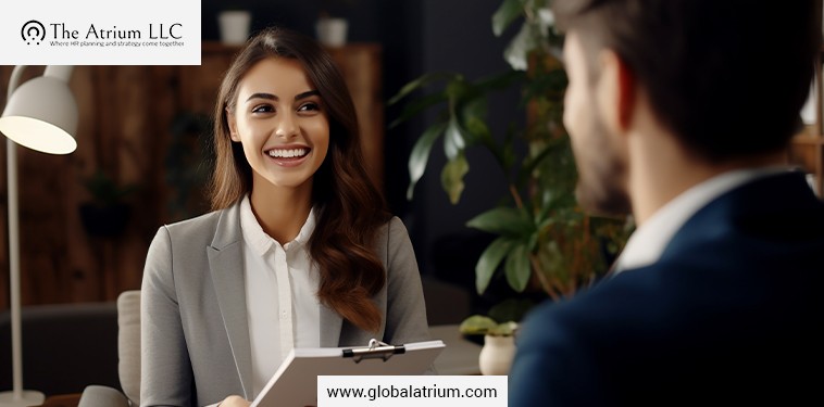 During a professional interview, a smiling candidate in a blazer reviews a clipboard while HR consulting guidance supports small business hiring decisions.